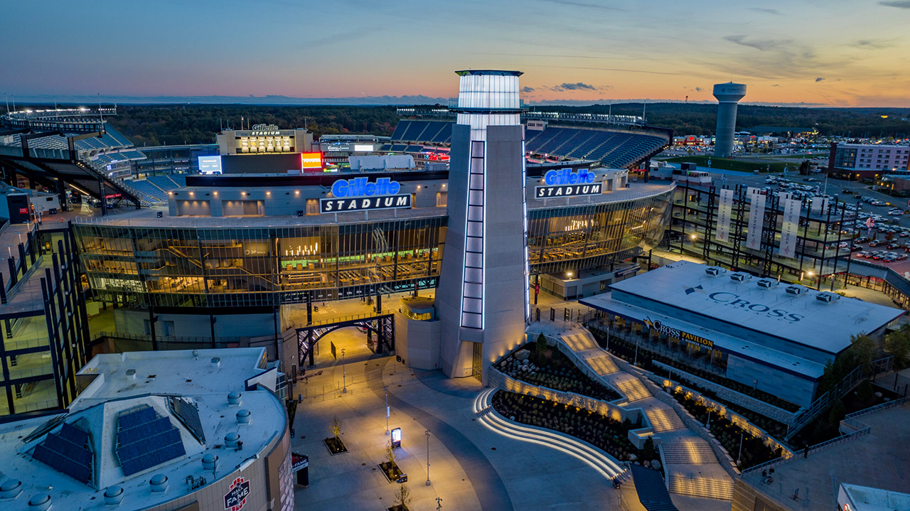 Aerial of Gillette Stadium at night showing the Lighthouse, the Cross Insurance Club, and the Patriot Place Plaza.